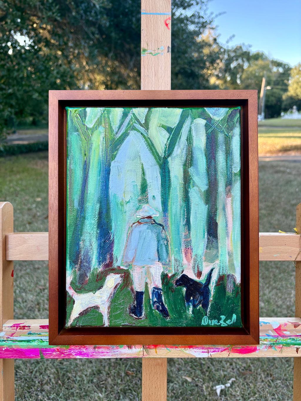 Three Good Friends displayed in a brown frame on an easel outdoors.