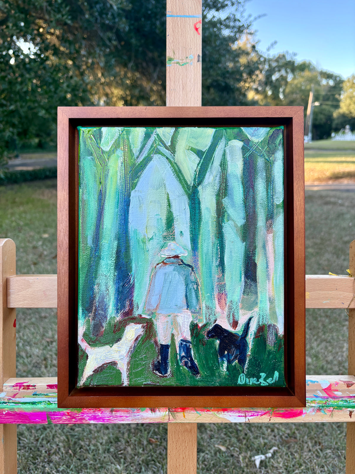 Three Good Friends displayed in a brown frame on an easel outdoors.